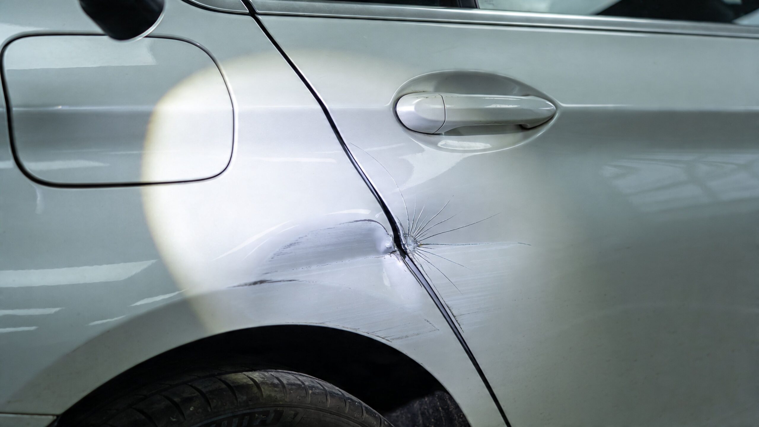 A close-up view of a damaged car door with a significant dent and paint scratches.