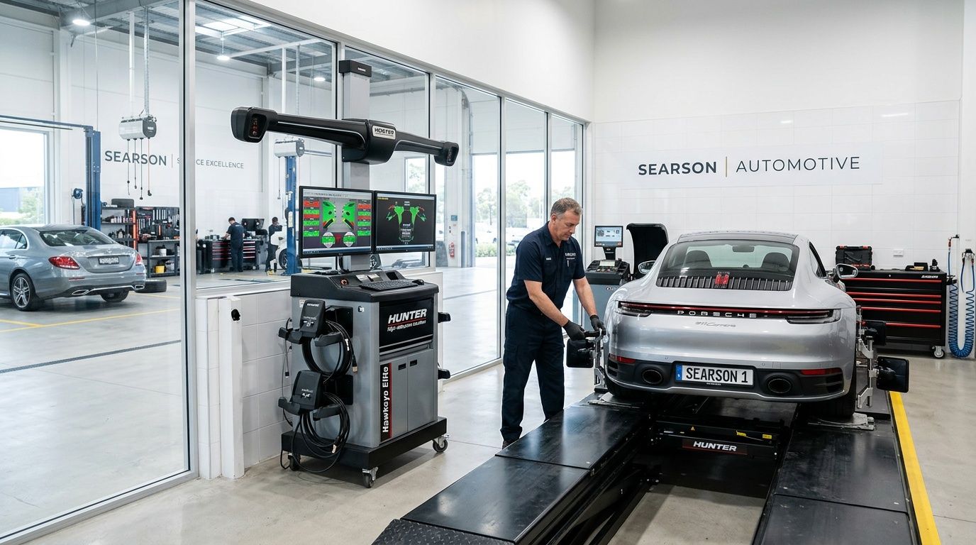 A professional automotive technician performs a precise wheel alignment on a silver Porsche sports car at a dealership.